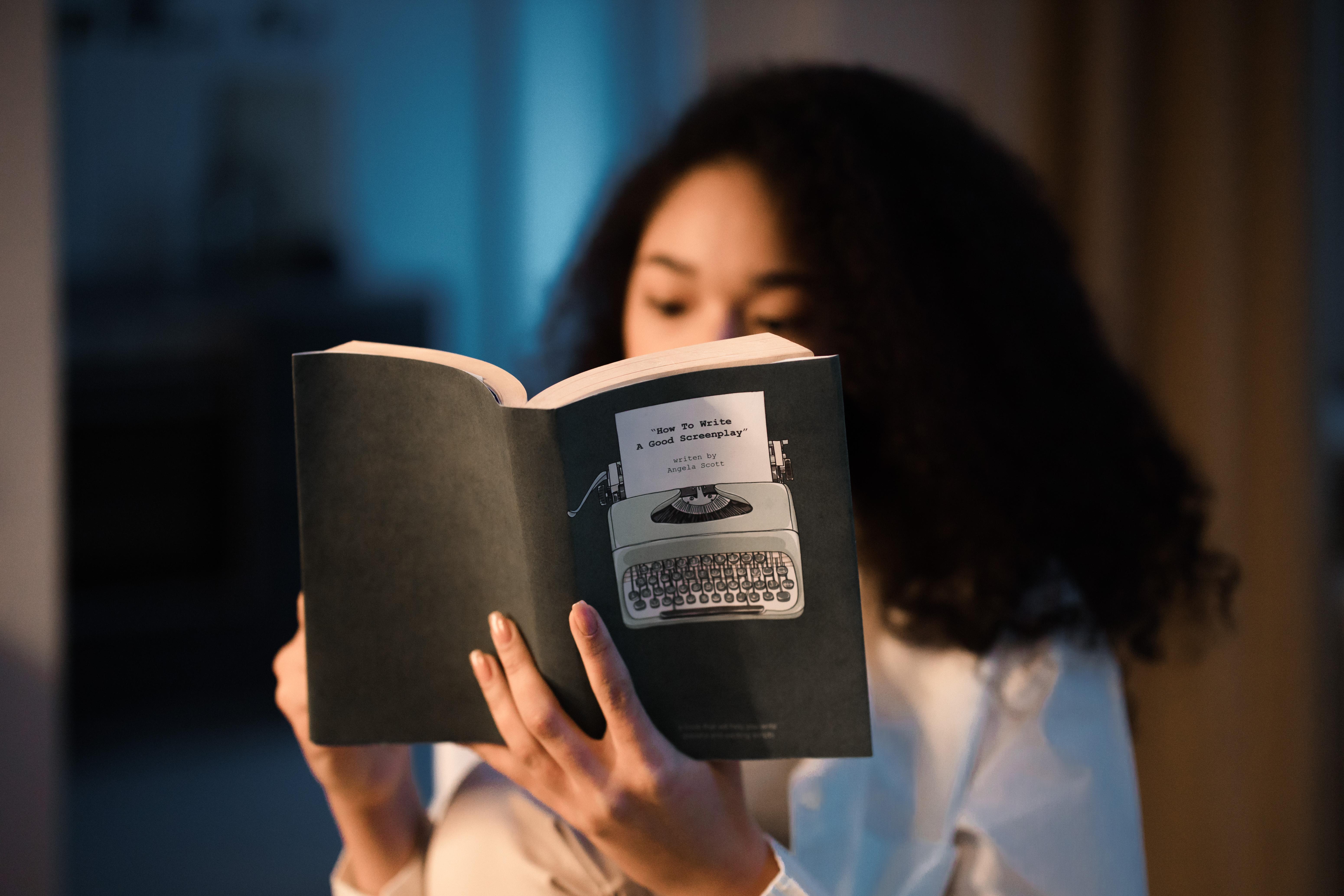 A young woman with curly hair sits in a dimly lit room, engrossed in reading a book. A young woman with curly hair sits in a dimly lit room, engrossed in reading a book.