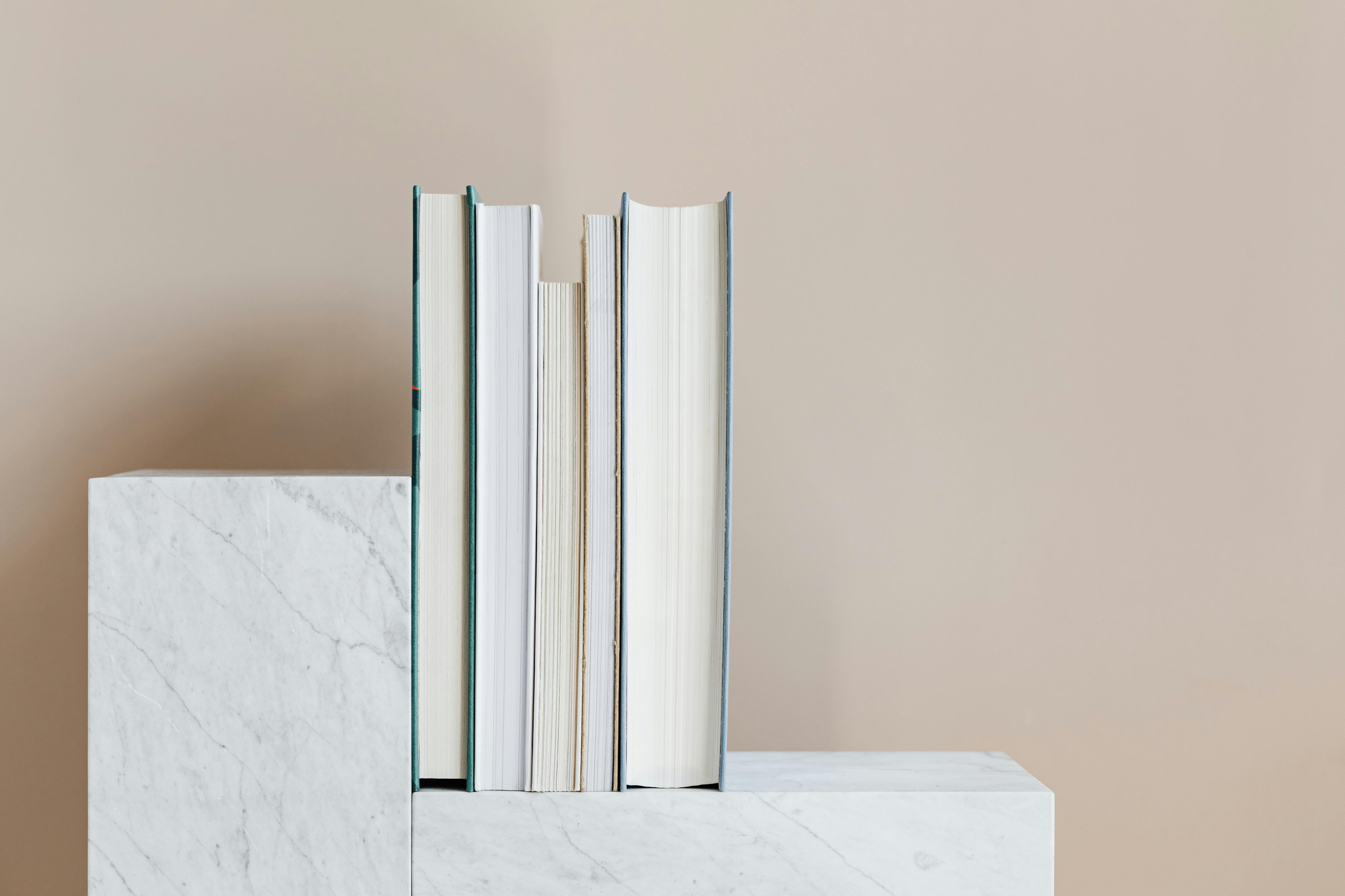 Hardcover books standing upright on a white marble surface against a neutral beige background.