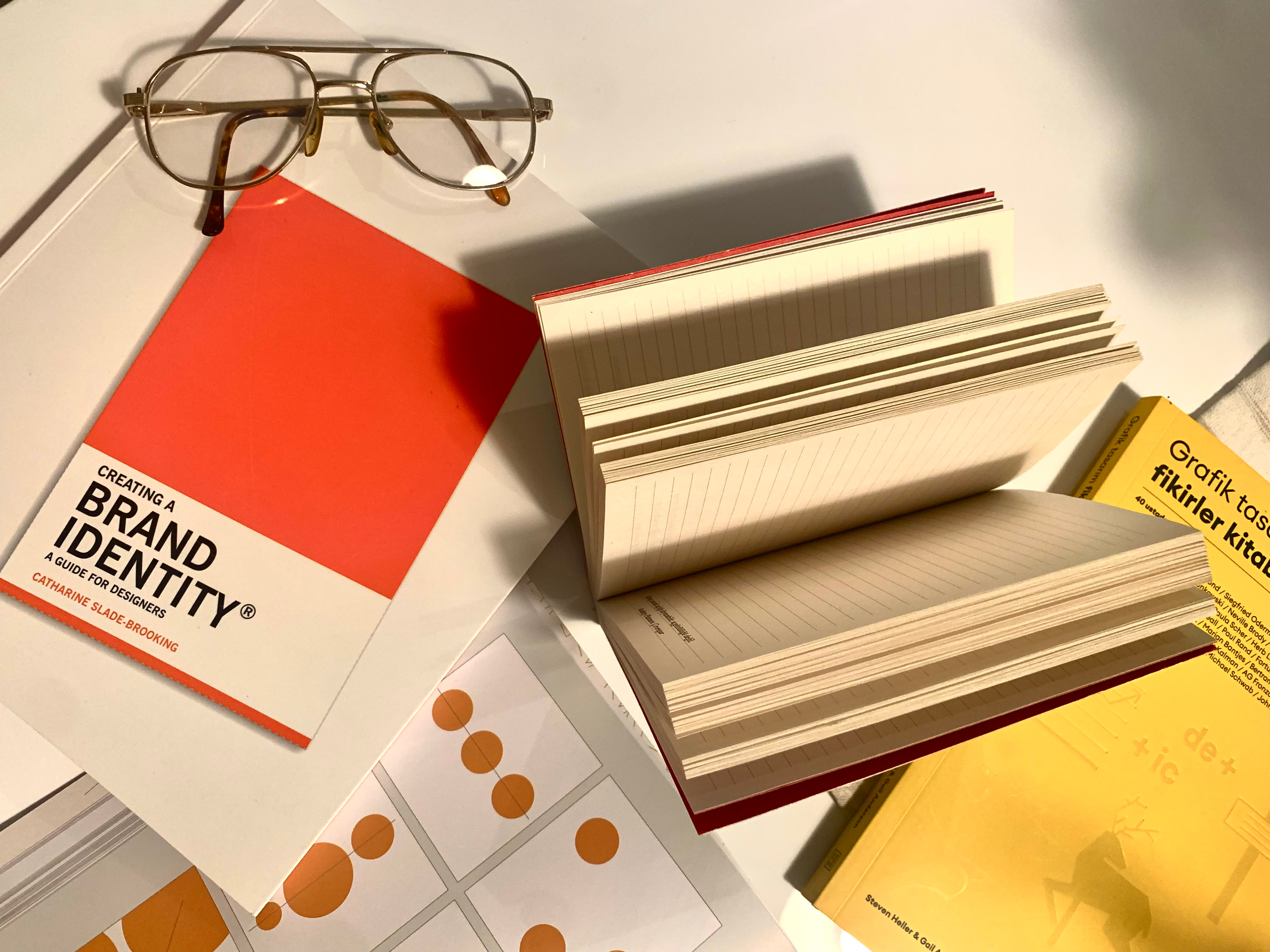 Flat lay of branding and design books with eyeglasses and open notebooks—representing cover design and visual branding tools for self-publishing authors.