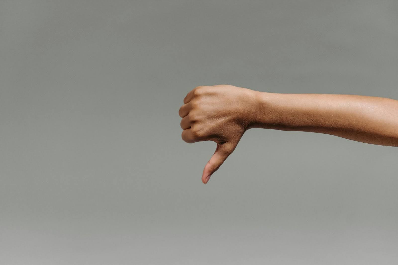 A hand making a thumbs down gesture against a neutral grey background, symbolising the negative impact of poor interview performance