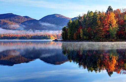 Scenic autumn forest reflecting on a calm lake with mist and mountain backdrop. Scenic autumn forest reflecting on a calm lake with mist and mountain backdrop.