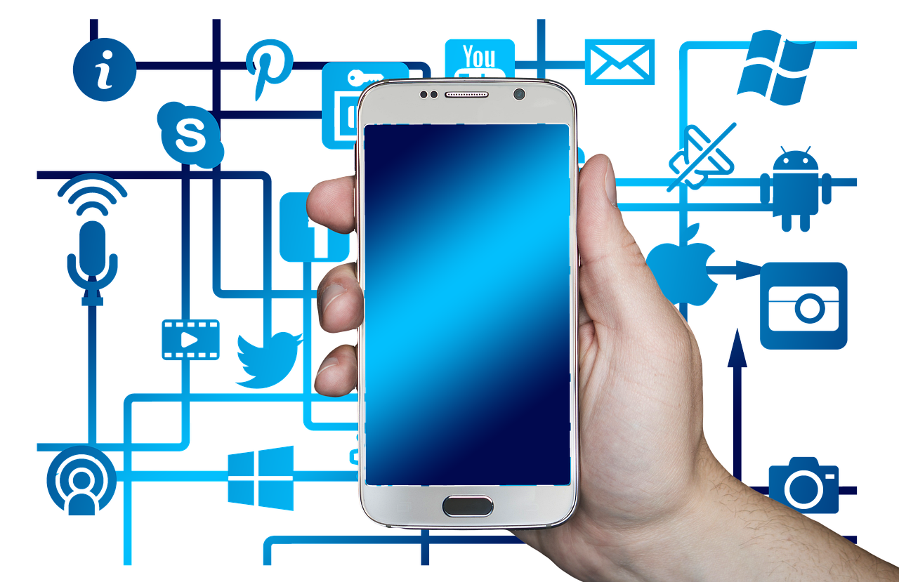A hand holding a smartphone with a blank blue screen surrounded by digital icons representing social media, communication, and technology integration, symbolizing the role of mobile technology in digital connectivity and business strategies. A hand holding a smartphone with a blank blue screen surrounded by digital icons representing social media, communication, and technology integration, symbolizing the role of mobile technology in digital connectivity and business strategies.