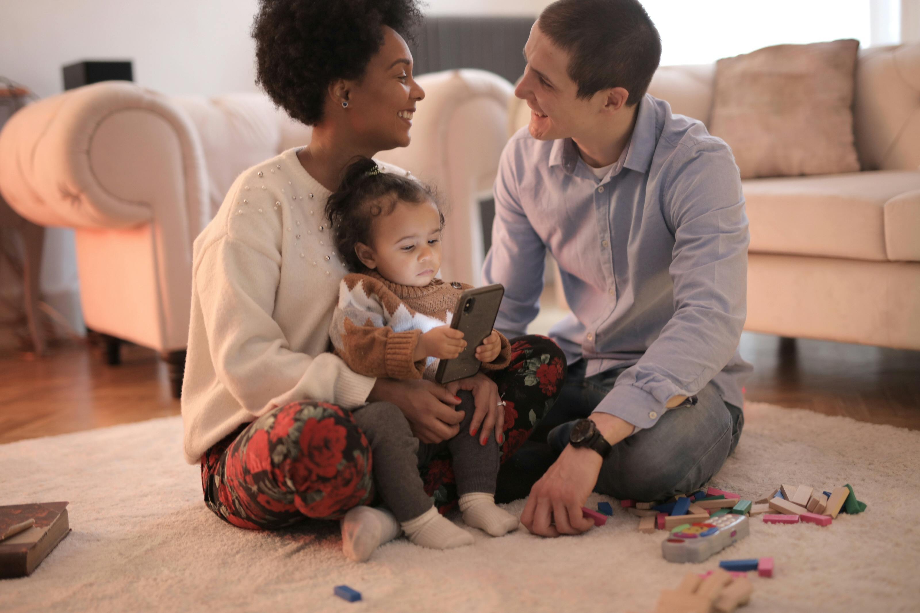 Family sitting together on the floor, the mom is holding their little girl while communicating with her husband.