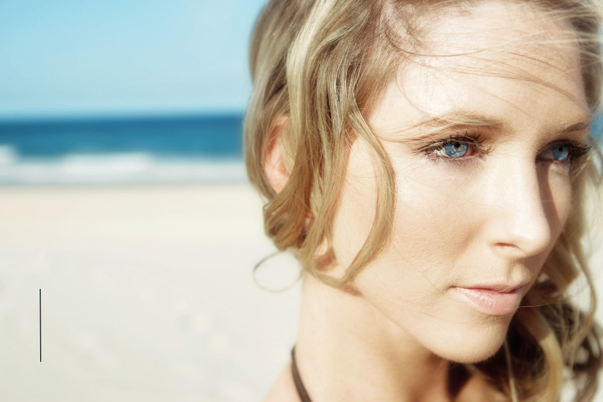 blonde woman with blue eyes looking off into the distance in front of the ocean blonde woman with blue eyes looking off into the distance in front of the ocean