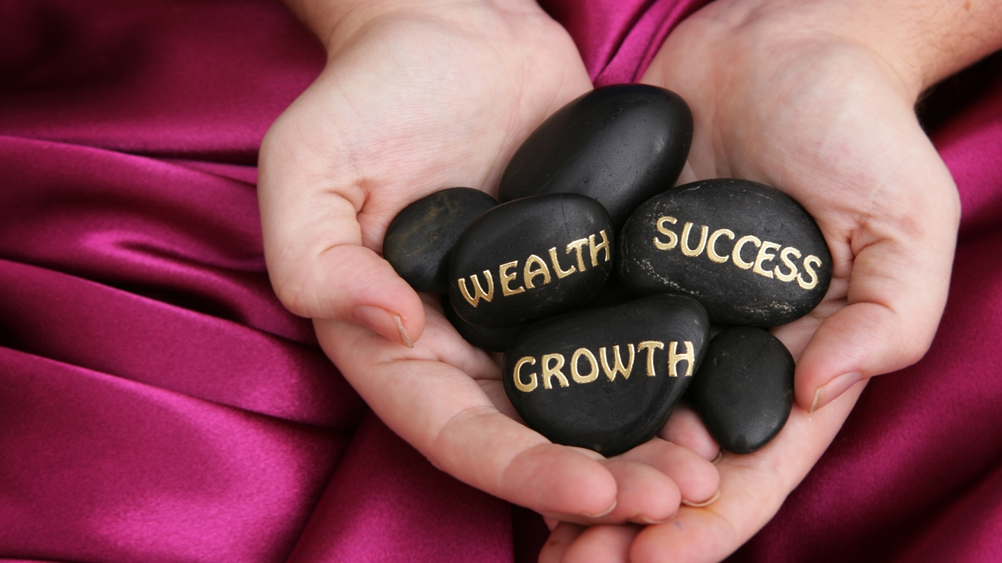 Hands holding black stones engraved with the words wealth, success, and growth. Hands holding black stones engraved with the words wealth, success, and growth.