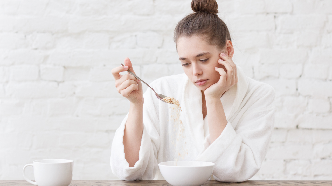 Woman in a white robe looking thoughtful while eating cereal in the morning. Woman in a white robe looking thoughtful while eating cereal in the morning.