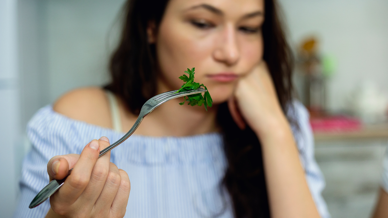 Woman with a fork holding fresh parsley, looking uninterested while eating. Woman with a fork holding fresh parsley, looking uninterested while eating.