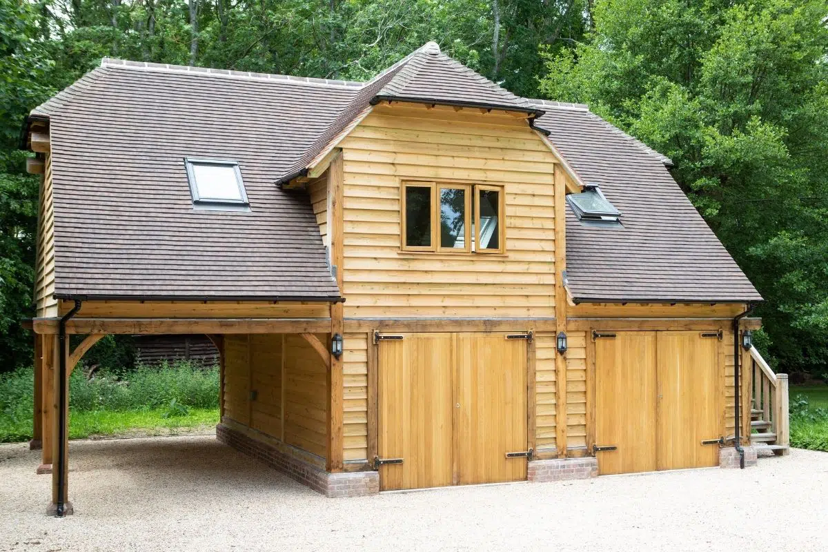 Oak-framed building with wooden cladding, sloped roof, skylights, and double garage doors, surrounded by greenery, illustrating traditional construction style relevant to oak conservatories.