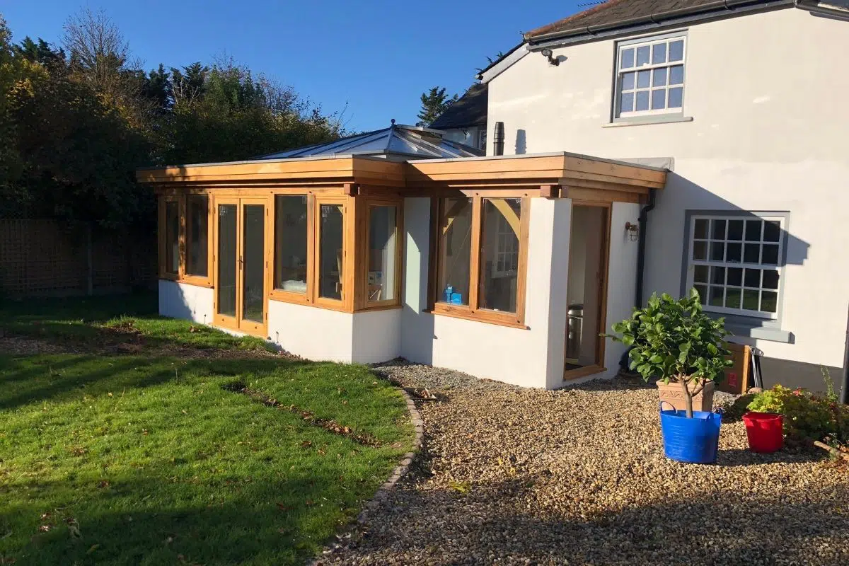 Glazed oak frame home extension showcasing traditional carpentry with large glass panels, surrounded by a garden and gravel pathway.