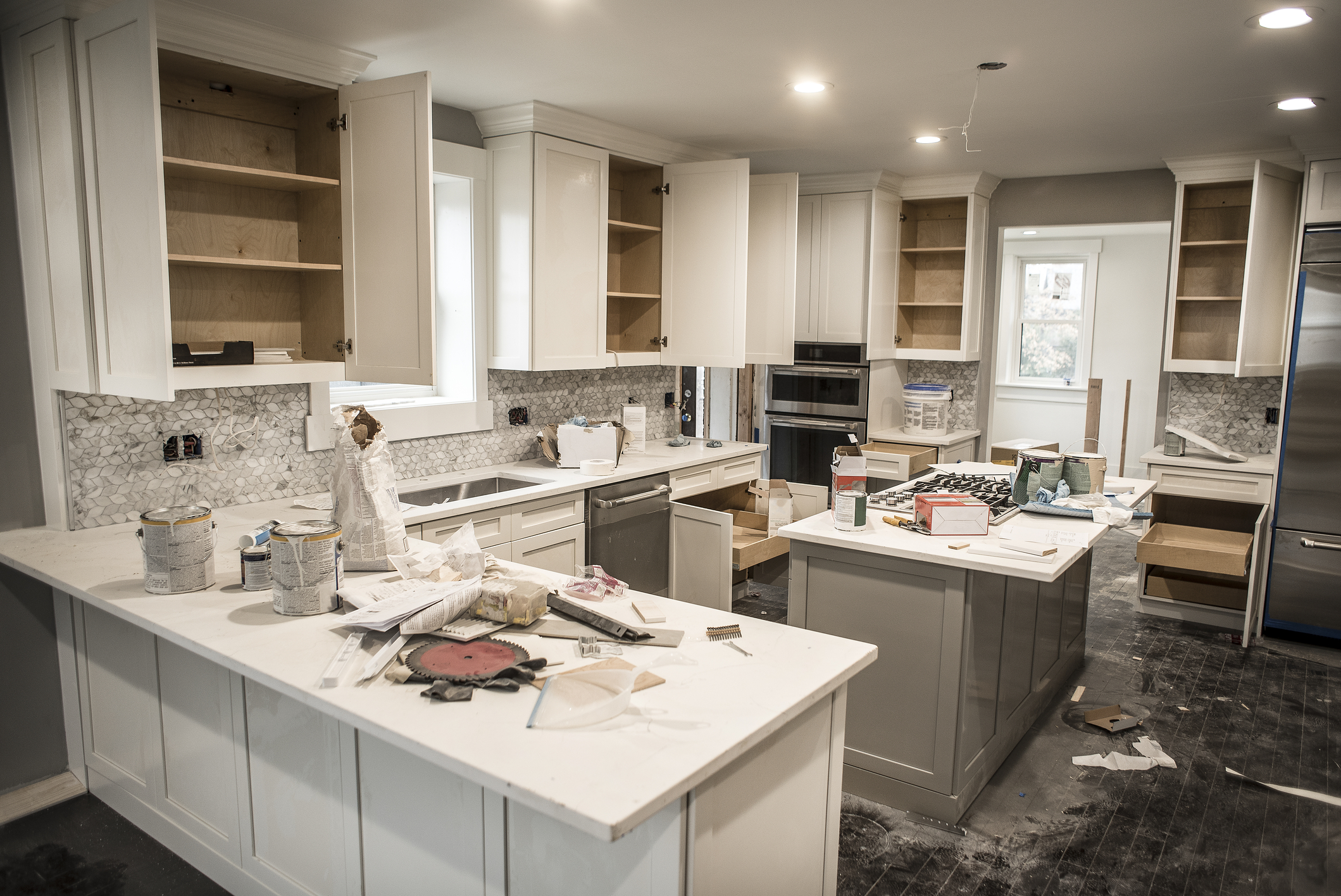 Messy home kitchen during remodeling with cabinet doors open cluttered with paint cans and tools, granite counter tops, appliances