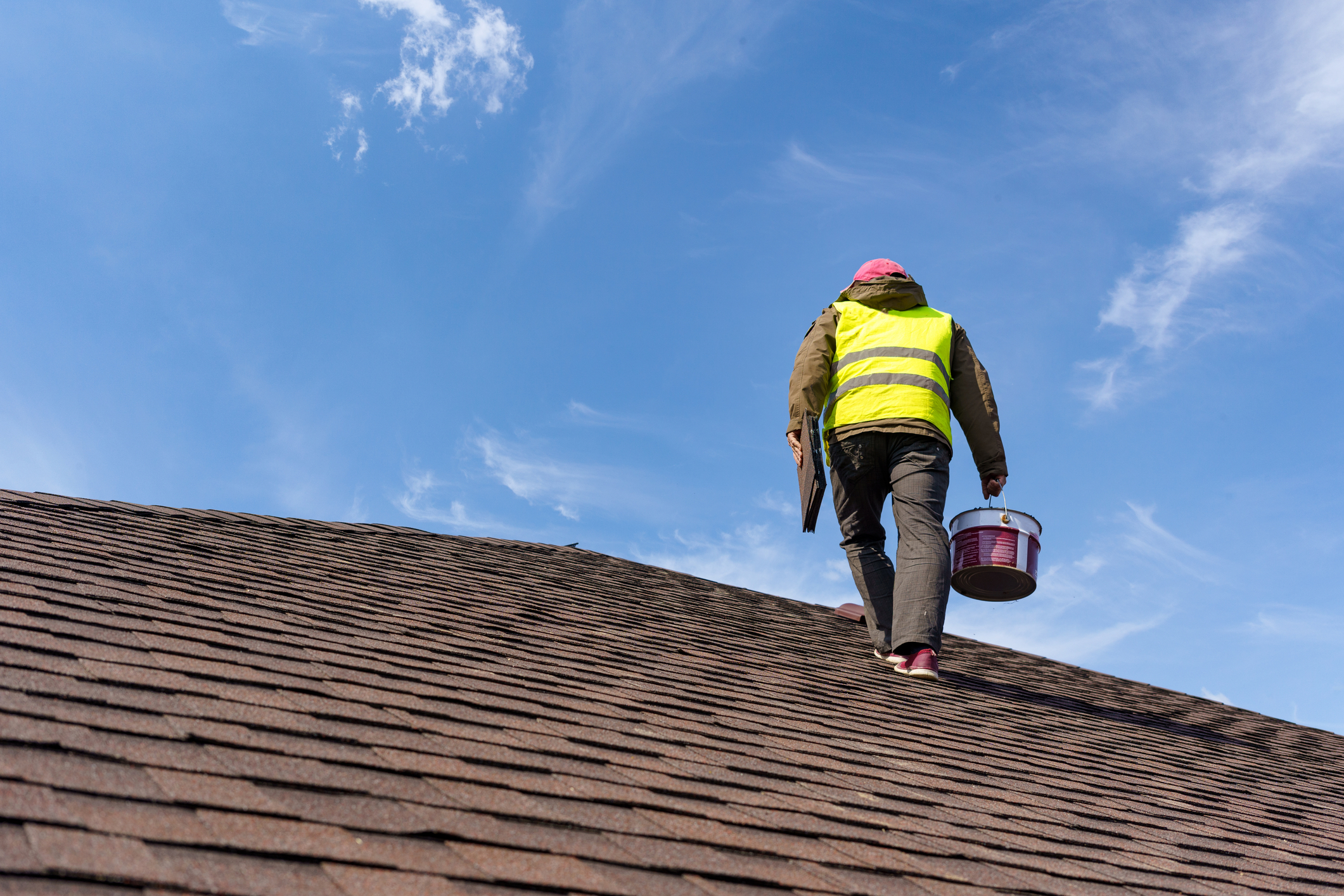 Unrecognizable and skilled workman in uniform standing on tile roof of new commercial building under construction with equipment and instrument