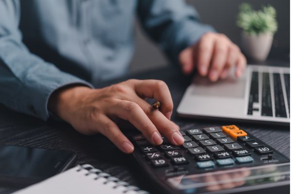 man using calculator with pen and laptop