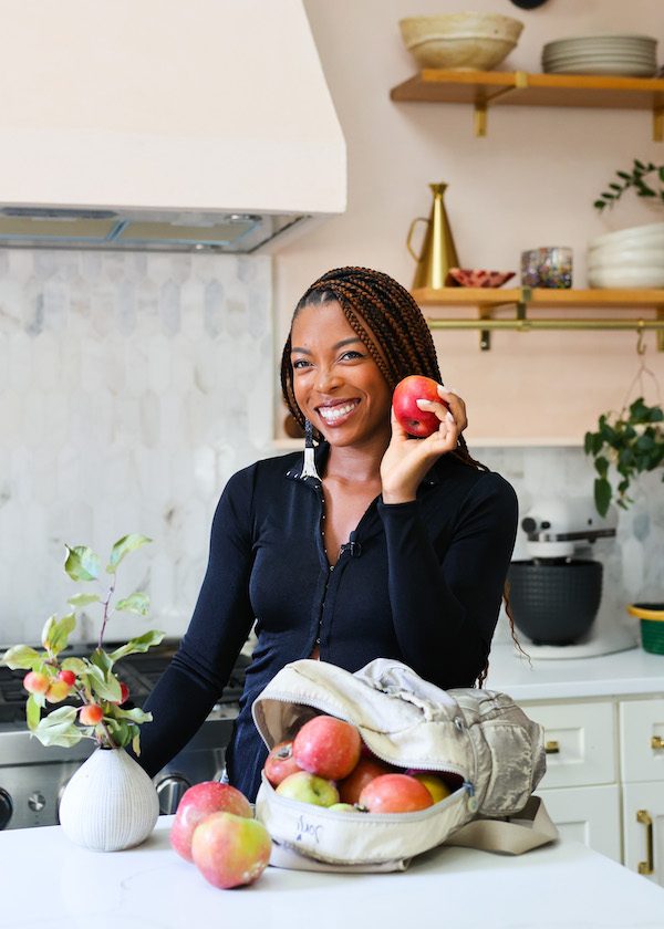 Photo of Jenné Claiborne in kitchen holding apple Photo of Jenné Claiborne in kitchen holding apple