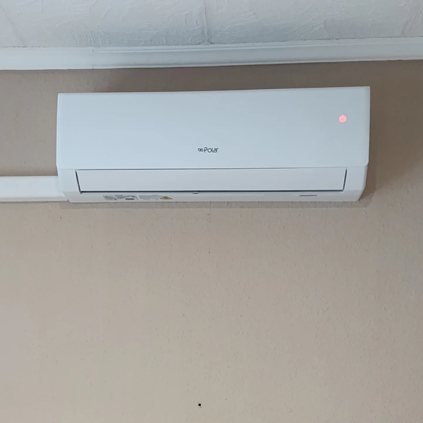 
Egy kikapcsolt, POLAR feliratú, beltéri klímaberendezés egy bézs falon.