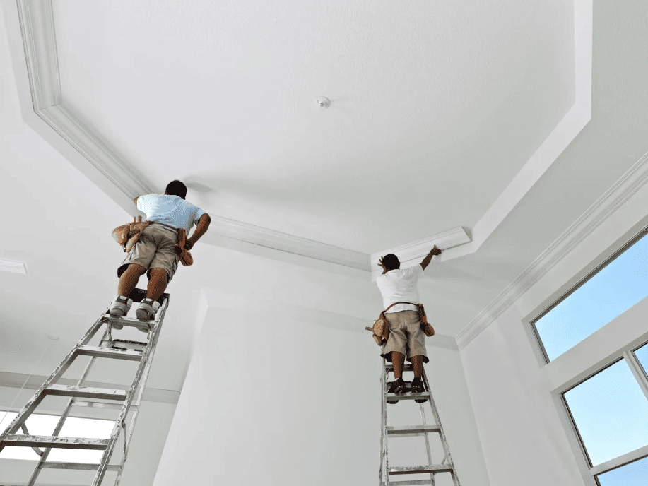 Workers on ladders performing water damage restoration on a ceiling.