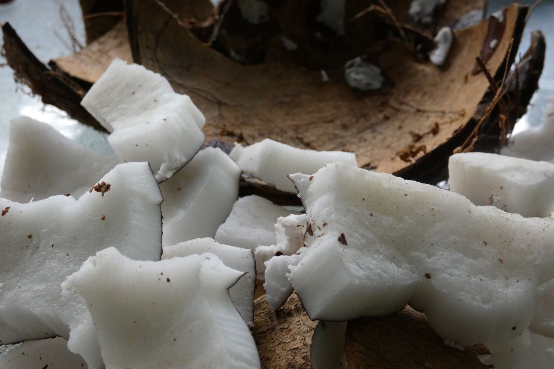 A pile of coconut meat next to a coconut shell A pile of coconut meat next to a coconut shell