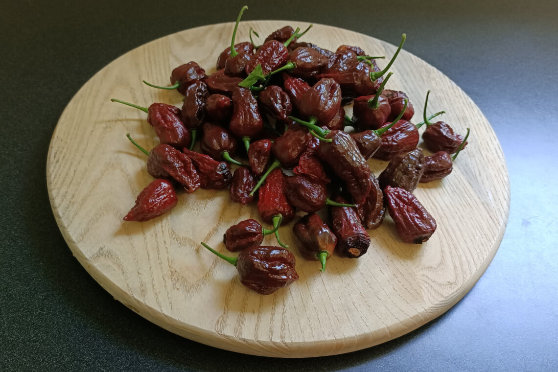 Fresh whole Chocolate Bhutlah peppers with dark brown, glossy, and bumpy skin arranged on a wooden chopping board Fresh whole Chocolate Bhutlah peppers with dark brown, glossy, and bumpy skin arranged on a wooden chopping board
