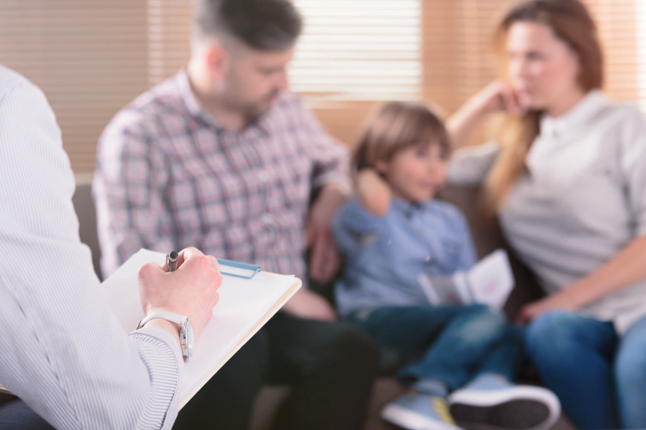 Counselor writing on a clip board, in the background a family sites on the couch
