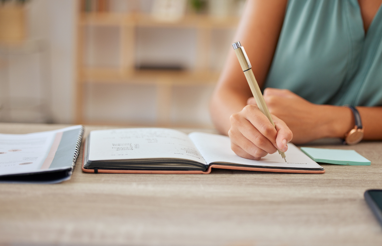 Person wearing a green shirt writing in a journal at a table