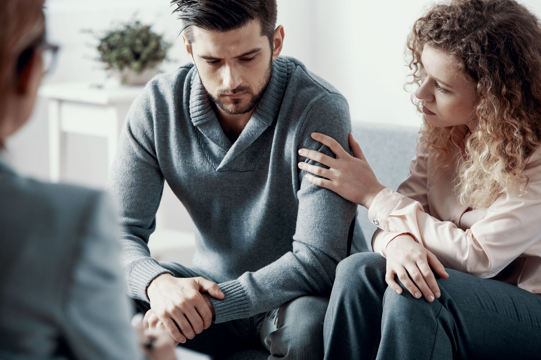 Sad couple on couch holding each other while talking to therapist. 
