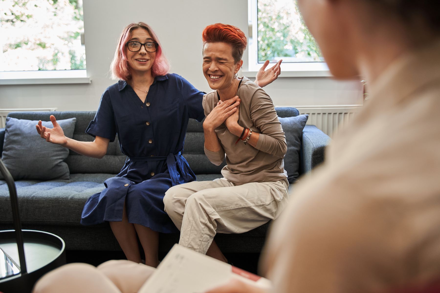 LBGTQ+ Couple on couch laughing while talking to therapist. 