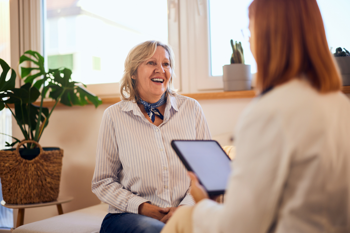 An older woman sits in front of her younger therapist who holds a tablet