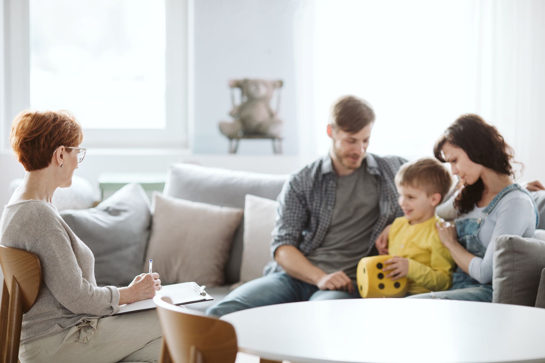 Father and mother on couch with young son across from woman with notepad and pen. 
