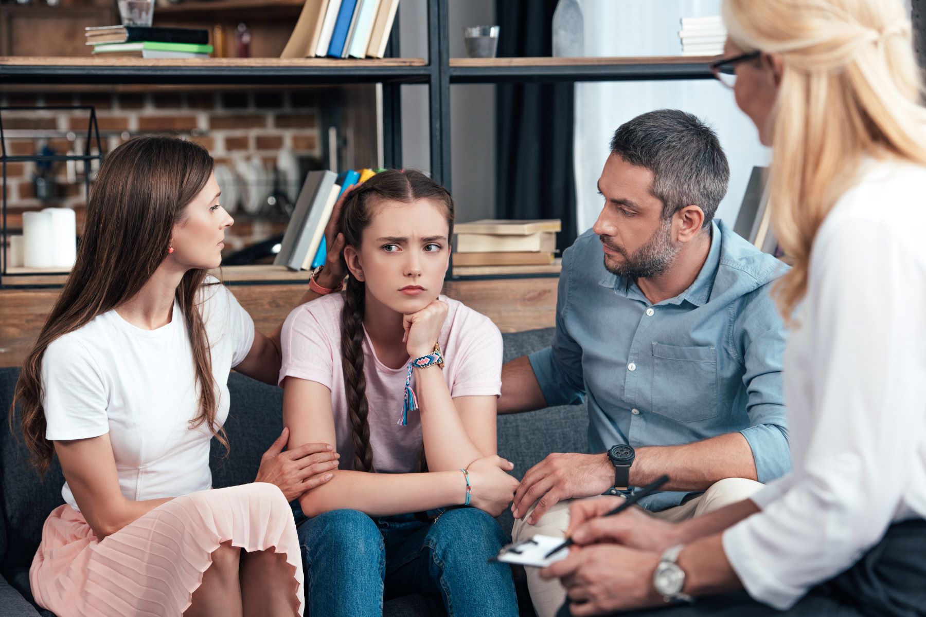 Family on couch supporting teenager daughter across from woman with notepad and pen. 