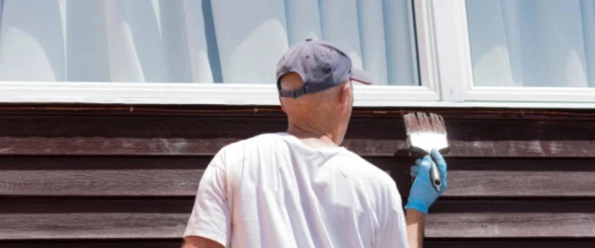 Man painting exterior wooden siding of house with white paint using brush. Man painting exterior wooden siding of house with white paint using brush.