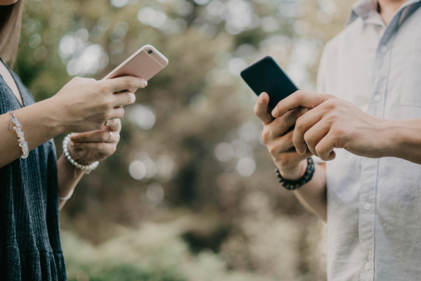 two people standing together on their phones not communicating