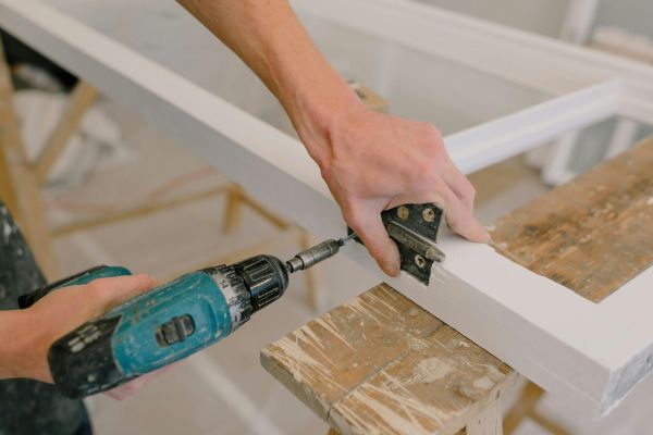 worker using a power drill to attach a hinge on a freshly painted wooden