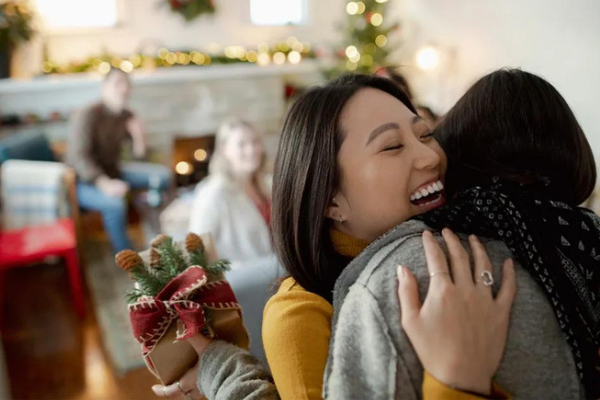 Two women embracing joyfully in front of a beautifully decorated Christmas tree.