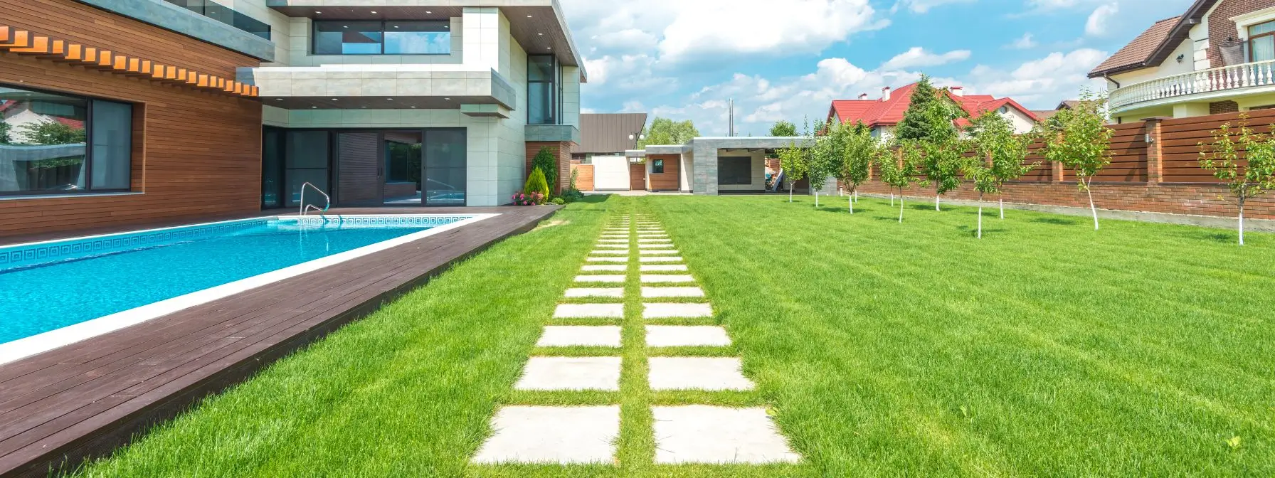Modern home with a lush, green lawn, neatly planted trees, and a backyard swimming pool, showcasing the results of effective year-round lawn care in a suburban Baltimore neighborhood. Modern home with a lush, green lawn, neatly planted trees, and a backyard swimming pool, showcasing the results of effective year-round lawn care in a suburban Baltimore neighborhood.