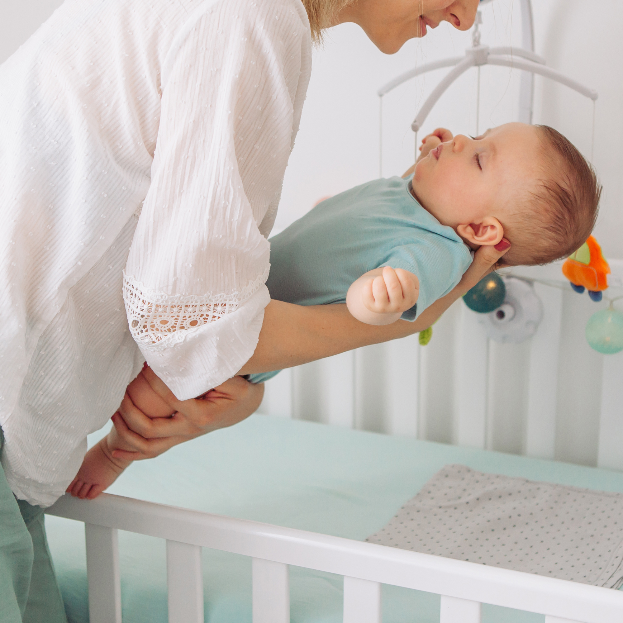 mum putting baby into a cot for sleep mum putting baby into a cot for sleep