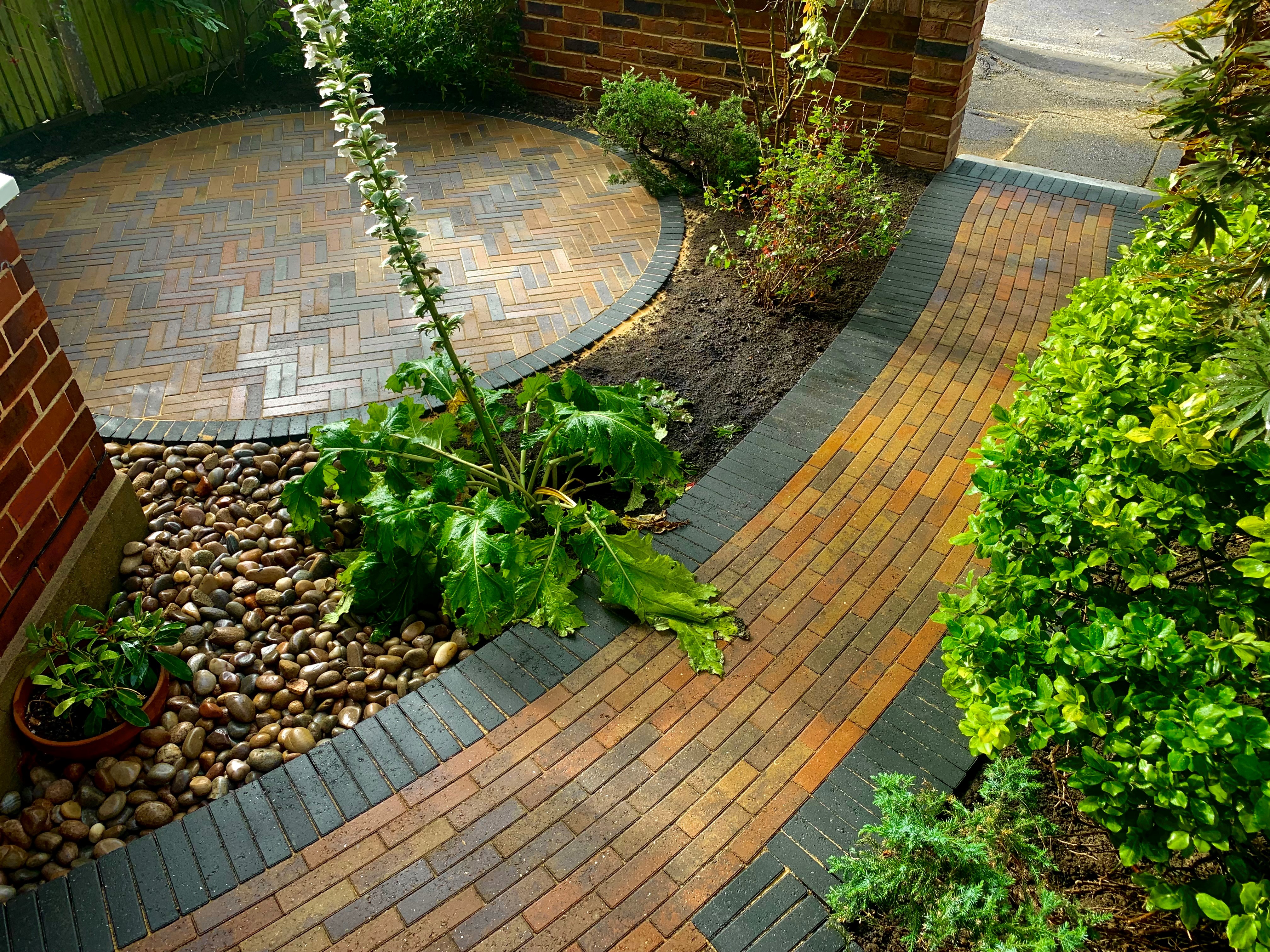 An inviting and beautifully designed block paved patio in Twickenham, surrounded by lush greenery. A well-crafted pathway leads to the house, with a captivating circular feature adding elegance to the landscape.