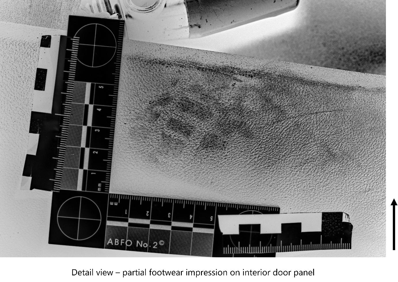High-contrast, negative image showing a detailed view of a partial footwear impression on a vehicle's interior door panel. The image includes an ABFO No. 2 forensic measurement scale for size reference and orientation, placed adjacent to the textured surface with the visible shoeprint. High-contrast, negative image showing a detailed view of a partial footwear impression on a vehicle's interior door panel. The image includes an ABFO No. 2 forensic measurement scale for size reference and orientation, placed adjacent to the textured surface with the visible shoeprint.