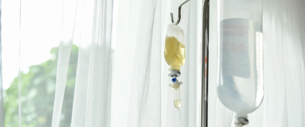 IV hydration therapy drip bag hanging near a window in a bright medical setting. IV hydration therapy drip bag hanging near a window in a bright medical setting.
