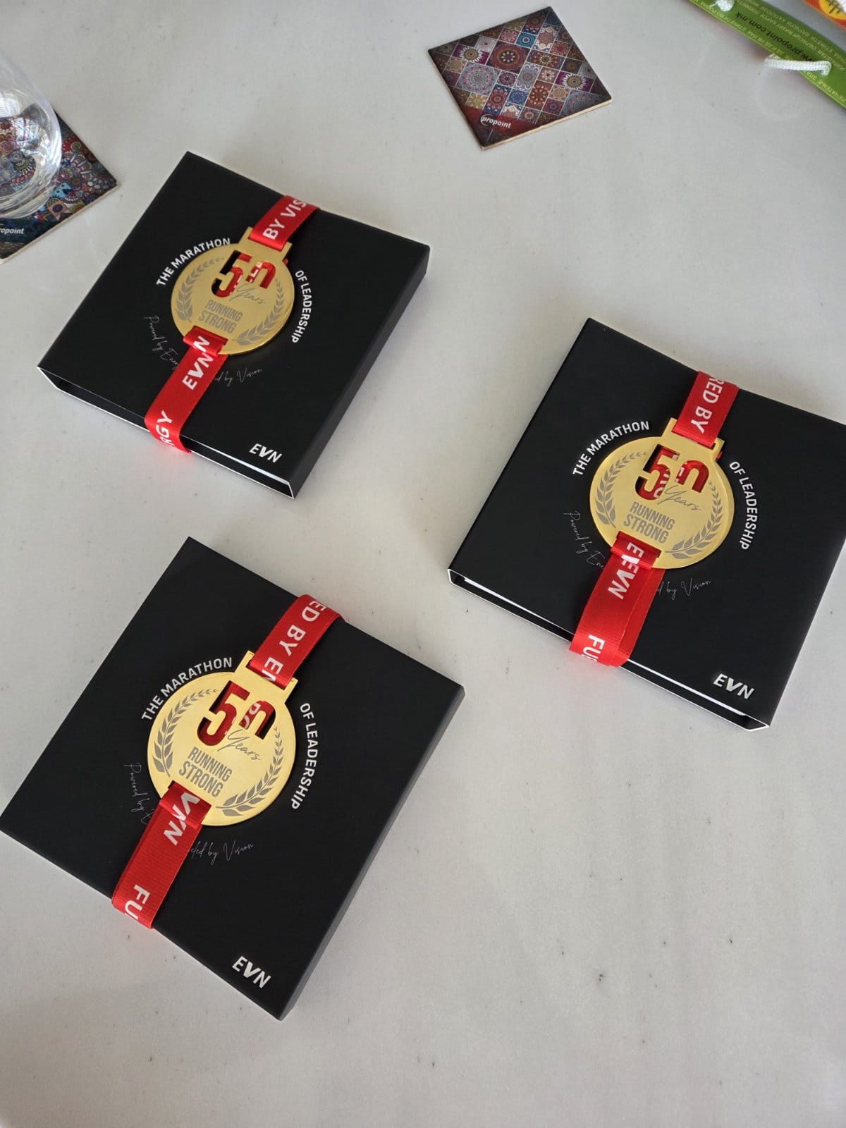 Three premium black gift boxes with red EVN ribbons and custom 24-carat gold commemorative medals designed by Opullex, celebrating 50 years of leadership with the ‘Running Strong’ theme—luxury packaging for a bespoke jubilee project.