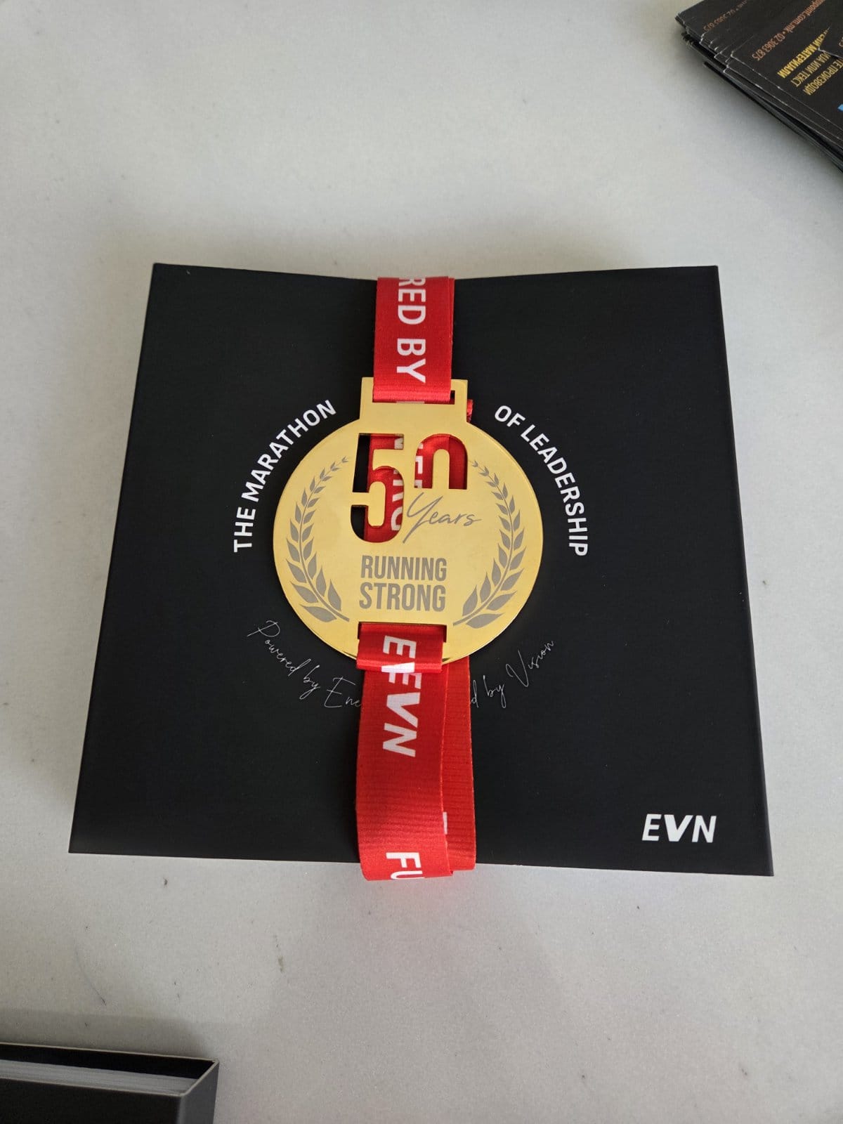 Three premium black gift boxes with red EVN ribbons and custom 24-carat gold commemorative medals designed by Opullex, celebrating 50 years of leadership with the ‘Running Strong’ theme—luxury packaging for a bespoke jubilee project. Three premium black gift boxes with red EVN ribbons and custom 24-carat gold commemorative medals designed by Opullex, celebrating 50 years of leadership with the ‘Running Strong’ theme—luxury packaging for a bespoke jubilee project.