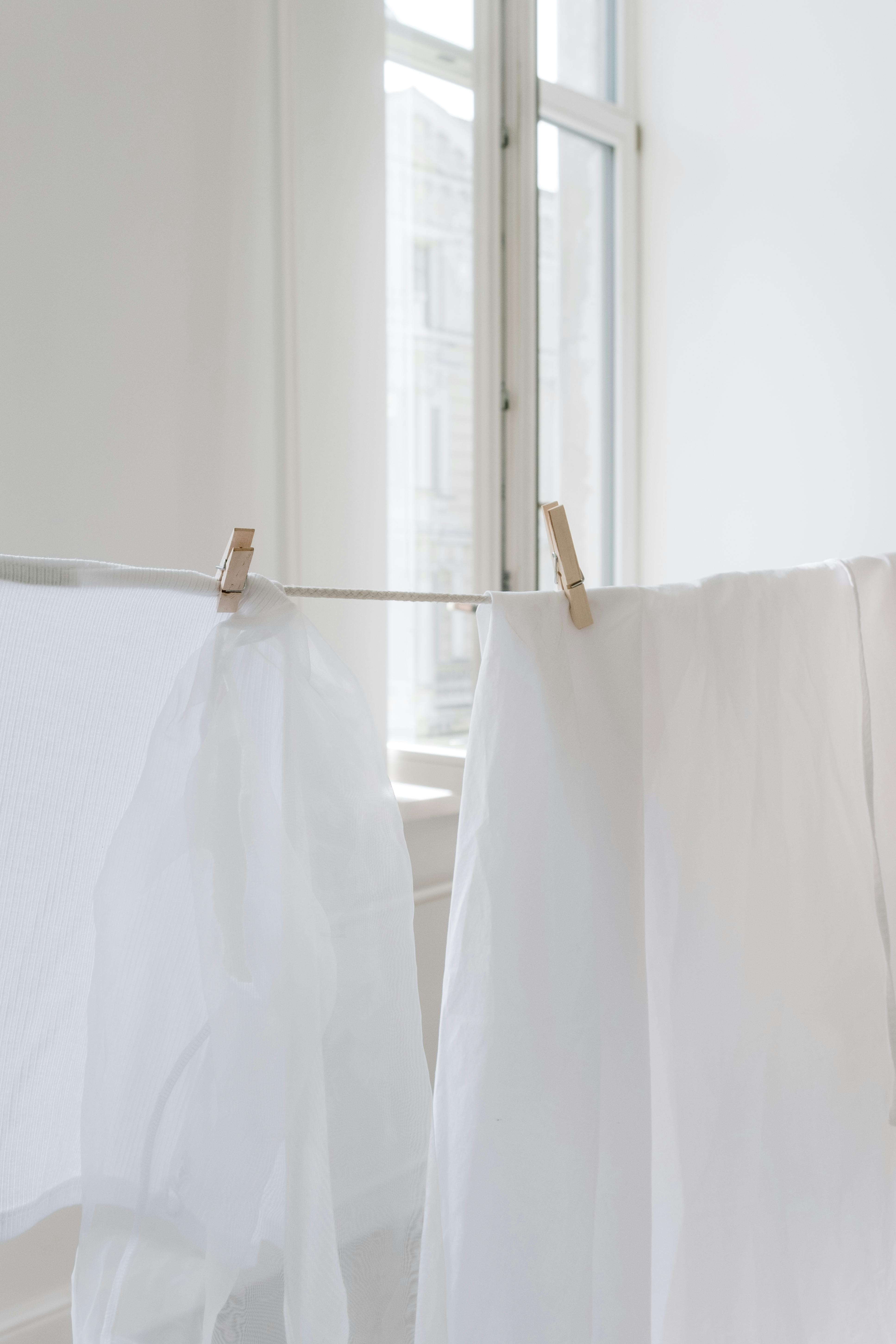Freshly washed white laundry hanging indoors on a clothesline with wooden clothespins near a bright window