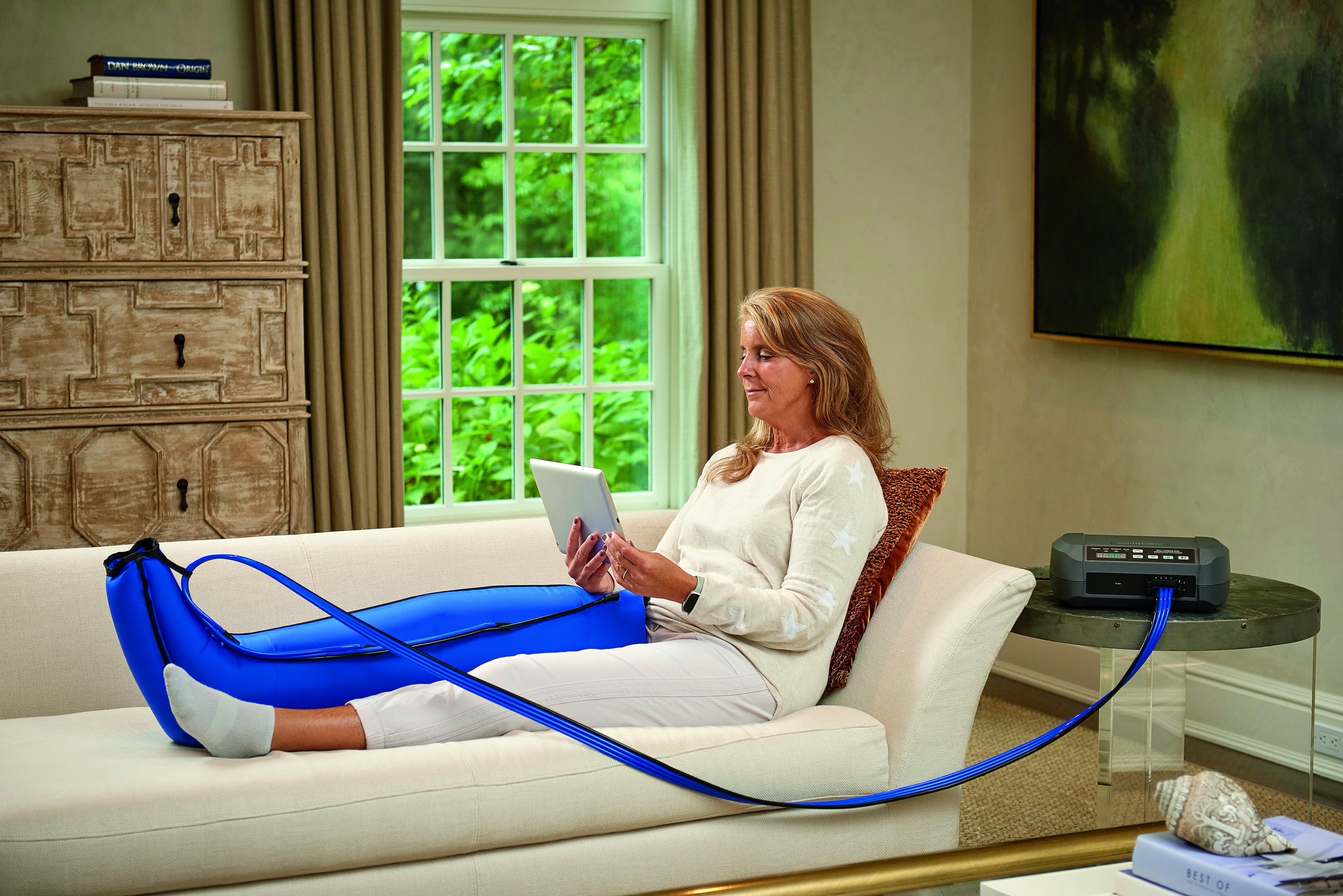 Woman using a pneumatic compression pump at home for lymphedema therapy, wearing blue leg sleeves while relaxing in a recliner—MCB DME compression equipment for at-home circulation support in New Jersey. Woman using a pneumatic compression pump at home for lymphedema therapy, wearing blue leg sleeves while relaxing in a recliner—MCB DME compression equipment for at-home circulation support in New Jersey.