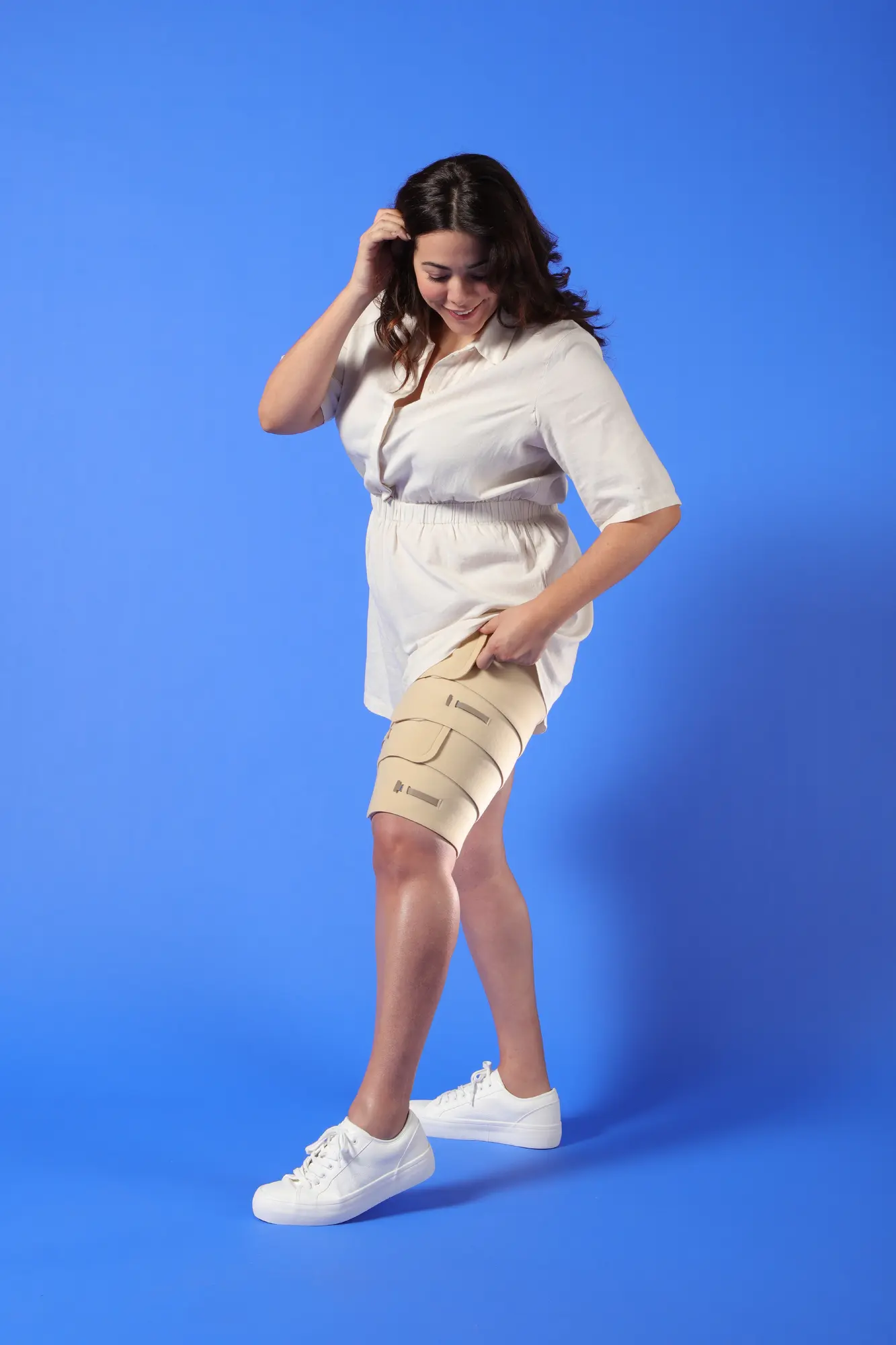 Woman demonstrating how to apply a beige adjustable thigh compression wrap designed for comfortable, customizable support.