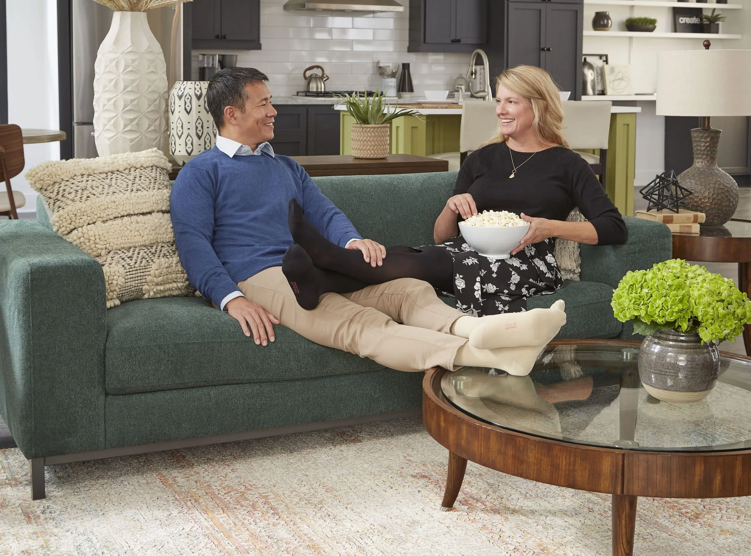 Middle-aged couple relaxing on a living room couch, wearing compression stockings, demonstrating everyday comfort and support during rest at home.