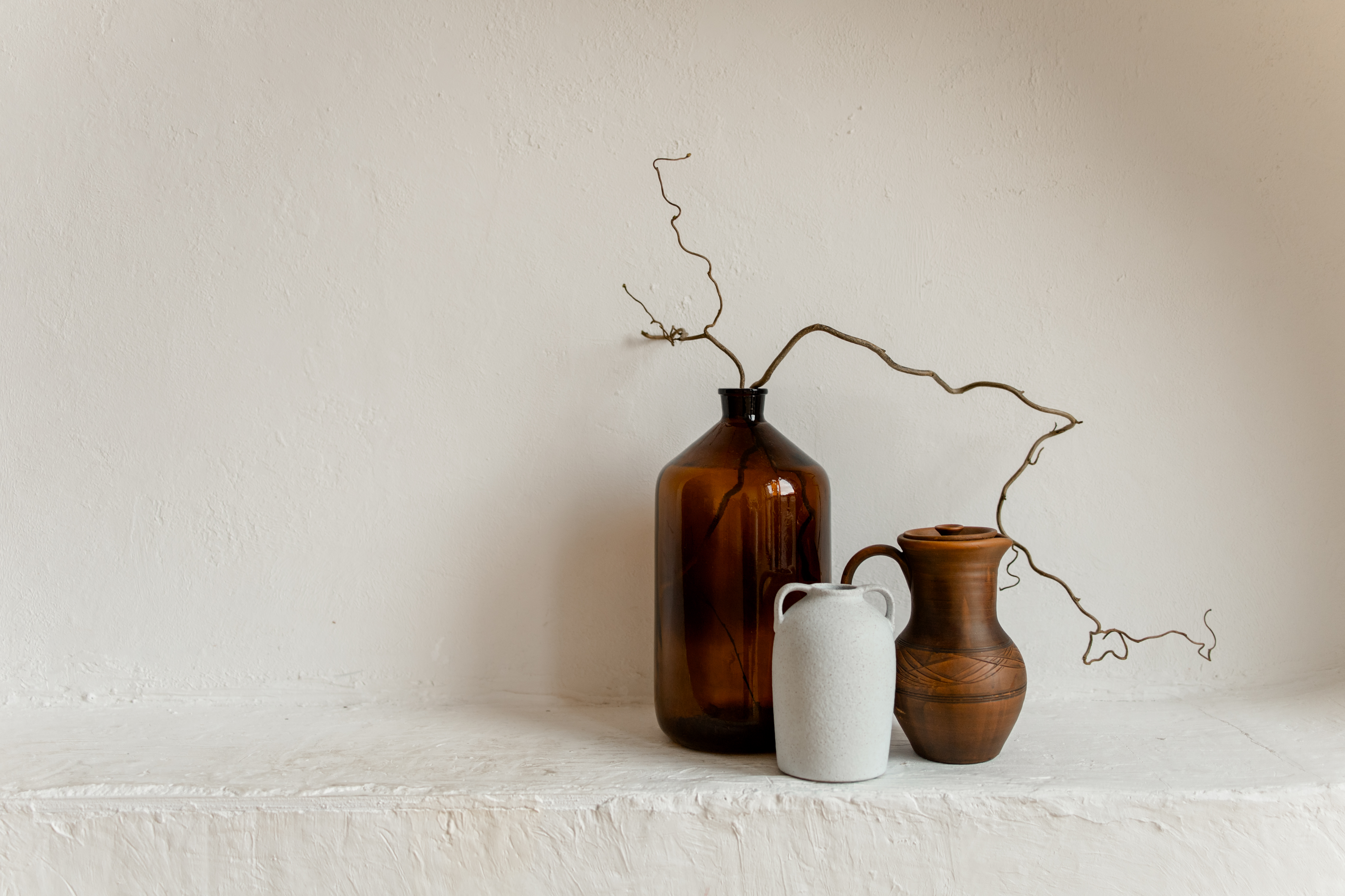 drei braune/beige Vasen, Ast vom Schnörkelstraucht vor weißer Wand