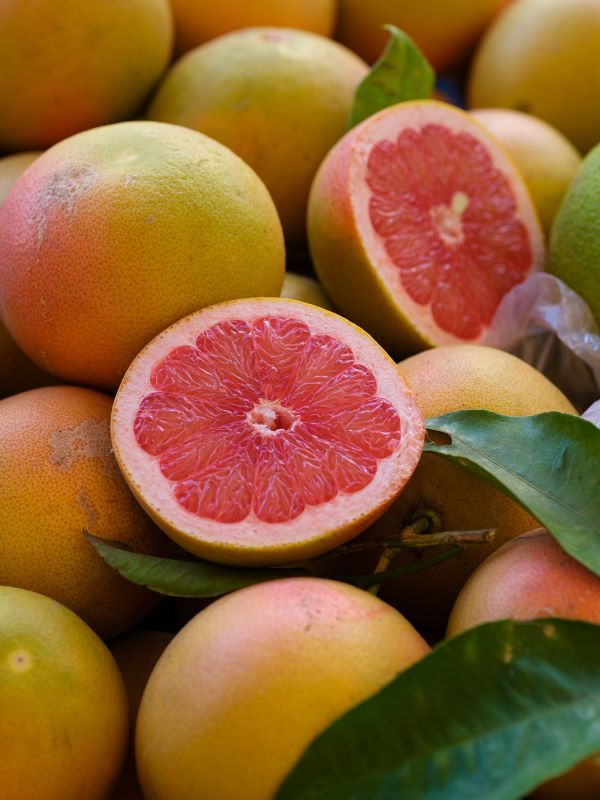 a pile of grapefruit with one cut grapefruit on top