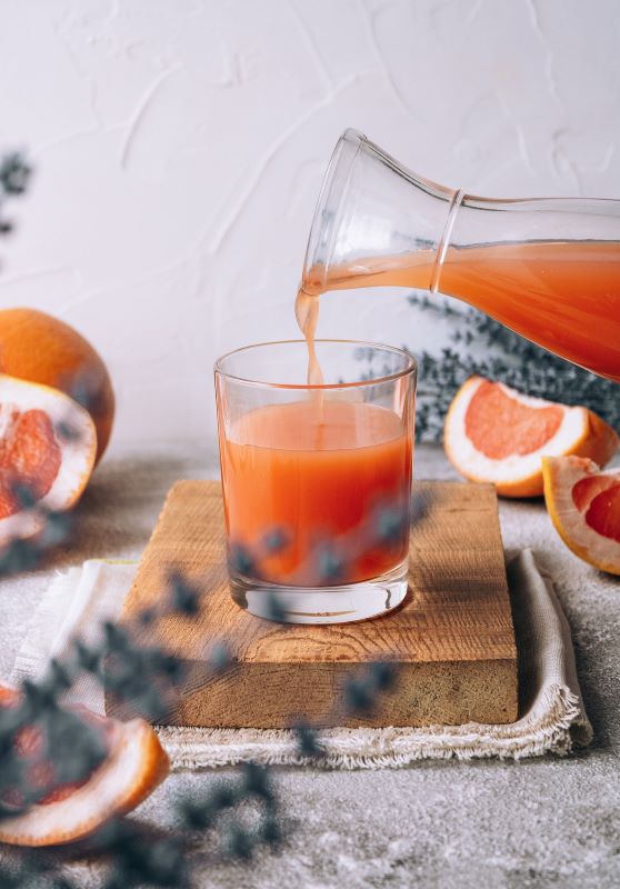 grapefruit juice being poured from a glass carafe into a glass which is sitting on a wooden board