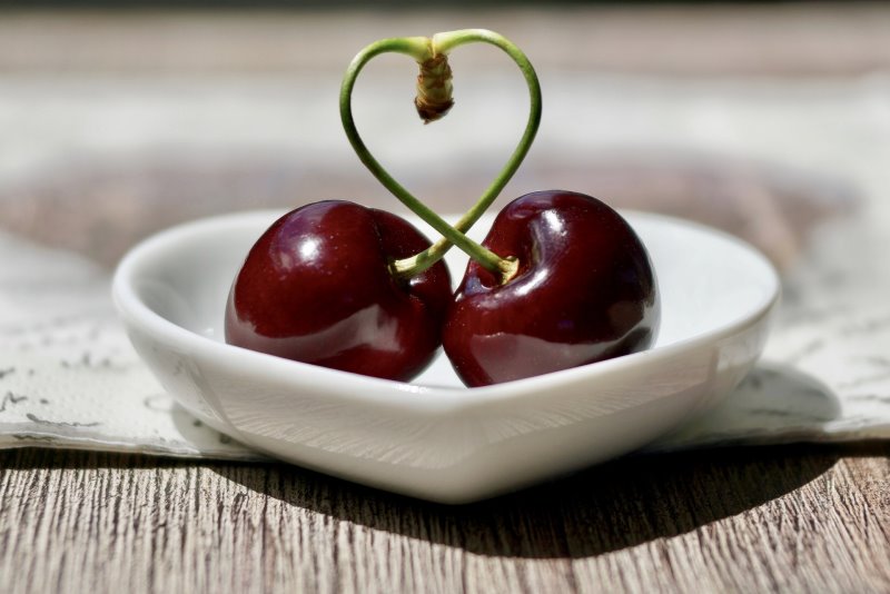 two cherries in a white bowl, the stems of the cherries are making a heart shape
