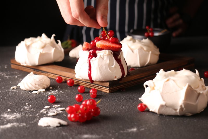 small meringues on a board with a hand placing redcurrents on top small meringues on a board with a hand placing redcurrents on top