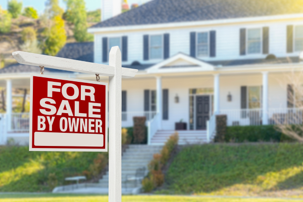 Charming summer home with blooming garden and 'For Sale' sign, showcasing peak selling season appeal.