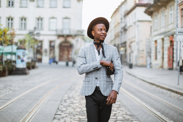 African man in stylish suit and hat walking on city street